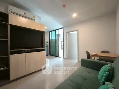 Modern living room with stylish furniture and open layout, featuring a cozy green sofa and sleek wooden cabinetry.