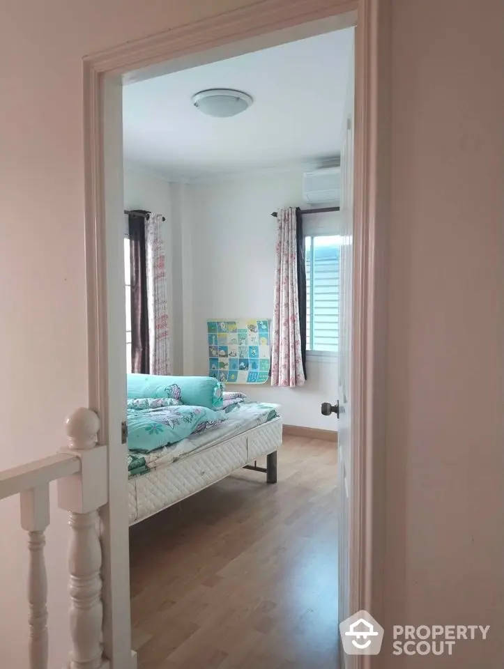 Inviting bedroom with polished hardwood floors, natural light, and charming curtains, perfect for relaxation and comfort in a cozy home setting.