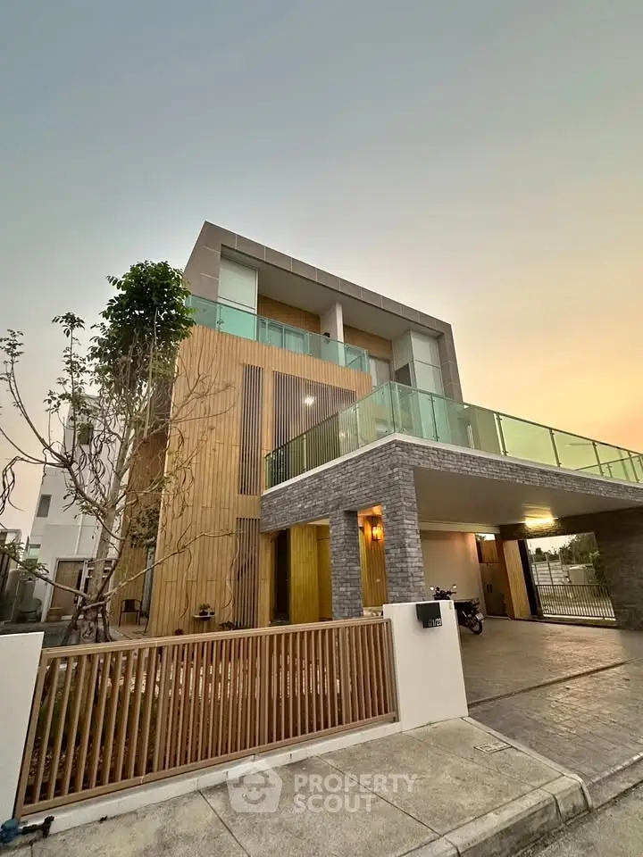 Modern three-story house with glass balconies and wooden accents at sunset.