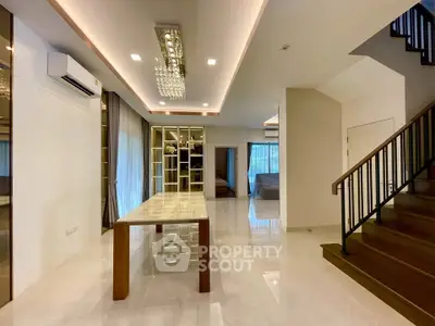 Spacious modern living room with elegant lighting and open layout, featuring a stylish staircase and large windows.