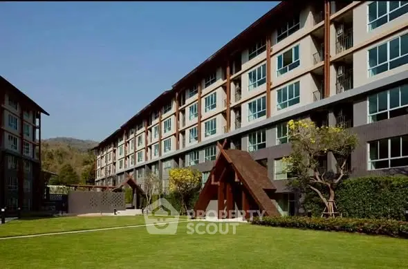 Modern apartment building with lush green lawn and scenic mountain backdrop.
