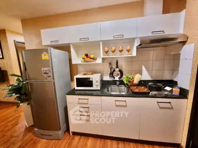 Modern kitchen with sleek cabinets, stainless steel fridge, and microwave in cozy apartment.
