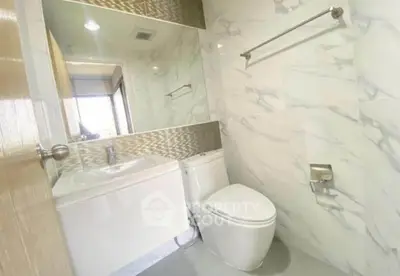 Modern bathroom with sleek design and marble tiles, featuring a toilet and sink.