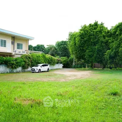 Spacious green lot with potential for development, adjacent to a residential building.