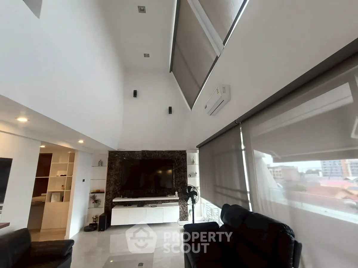 Spacious modern living room with high ceilings and large windows, featuring sleek furniture and a stylish entertainment center.