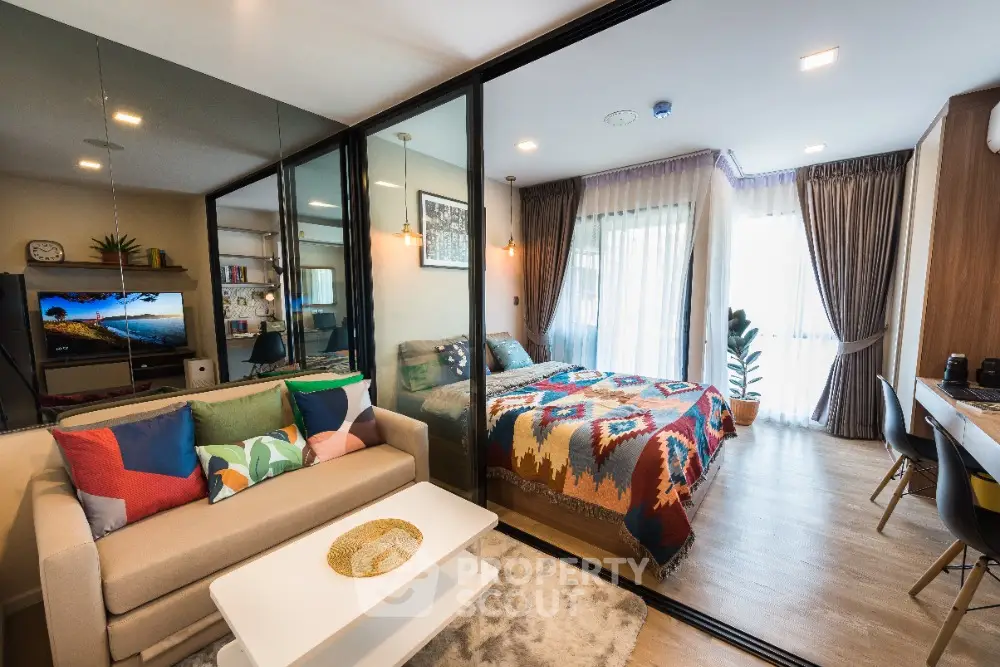 Modern studio apartment with colorful decor and glass partition separating living and bedroom areas.