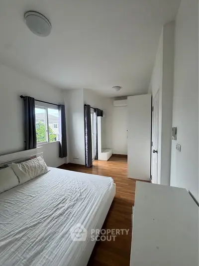 Spacious bedroom with large windows and wooden flooring in modern apartment.