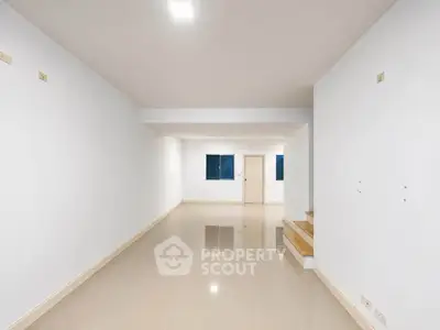 Spacious empty room with glossy tiled floors and staircase, ideal for customization.