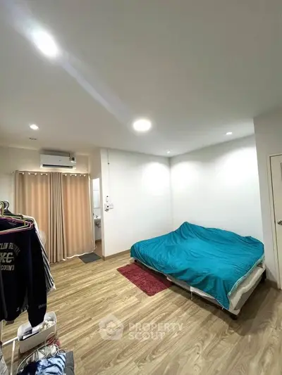Spacious bedroom with wooden flooring and modern lighting, featuring a cozy bed and air conditioning.