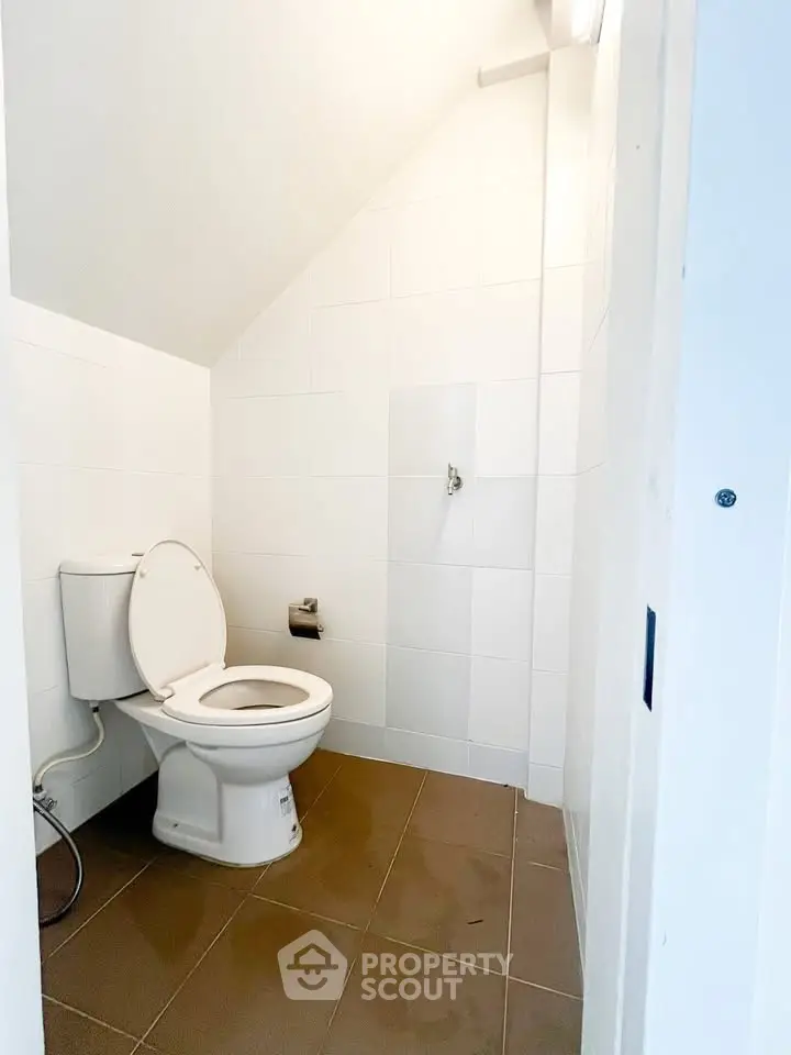 Compact white-tiled bathroom with sloped ceiling and modern toilet.