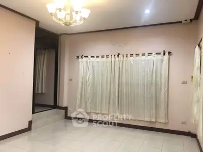 Spacious living room with elegant chandelier and large windows with curtains.