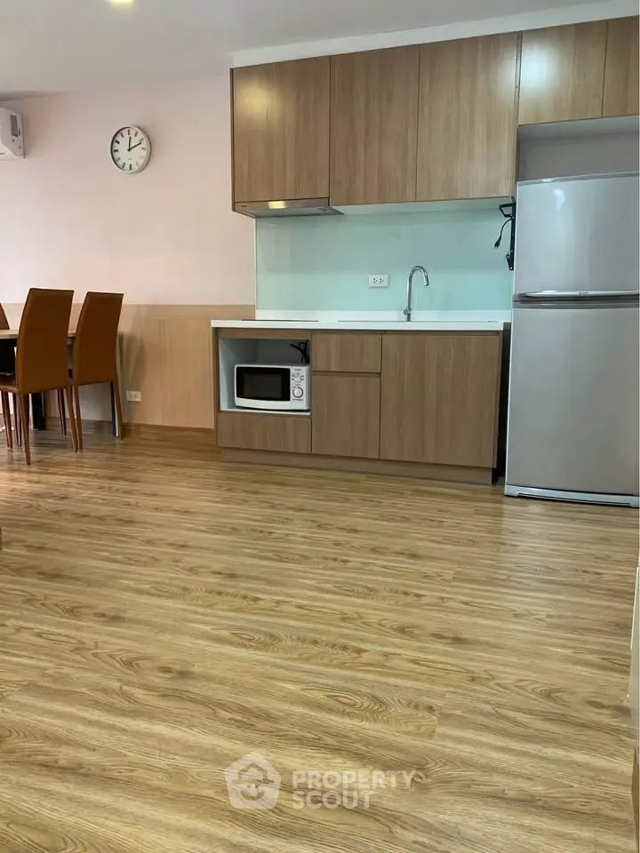 Modern kitchen with wooden cabinets and dining area, featuring a microwave and fridge.