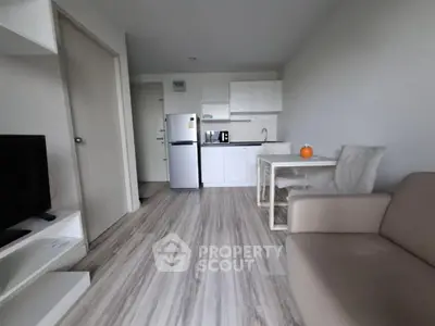 Modern open-plan living room with kitchenette and dining area, featuring sleek design and neutral tones.