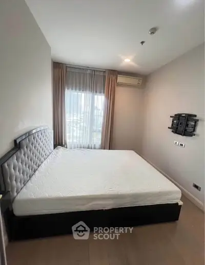 Spacious bedroom with large window and modern furnishings in a high-rise apartment.