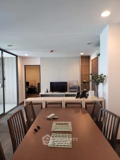 Spacious modern dining area with wooden table and chairs, open layout to living room with TV and decor.