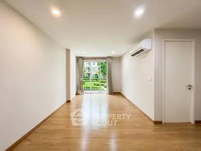 Spacious empty living room with wooden flooring and large window view.
