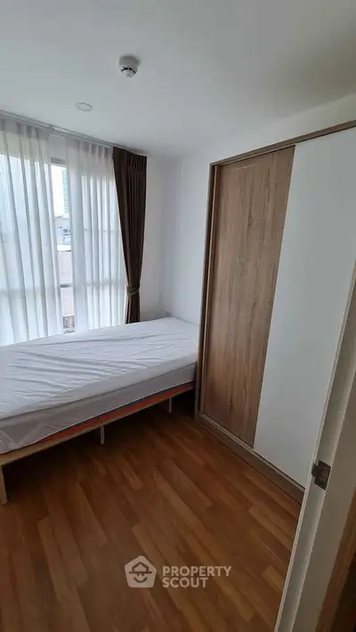 Cozy minimalist bedroom with wooden flooring and large window for natural light.