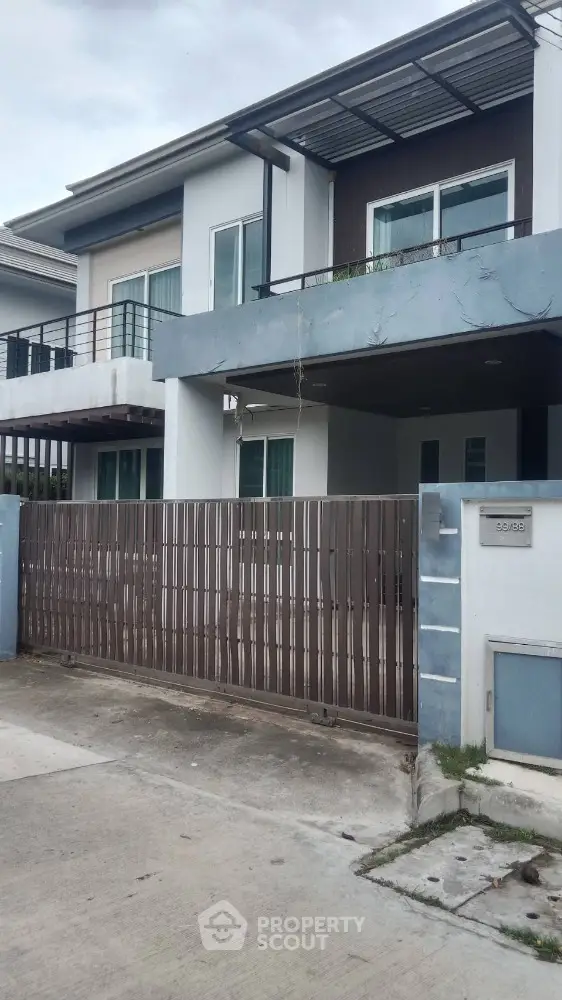 Modern two-story house with balcony and gated entrance in suburban neighborhood.