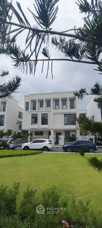 Elegant modern townhouse with lush green garden and parked cars in a serene neighborhood.