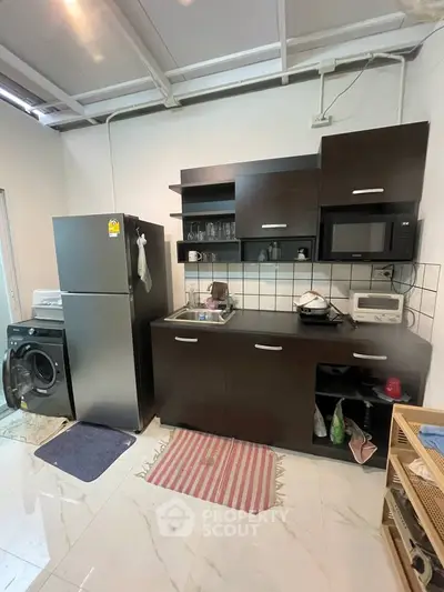 Compact kitchen with dark cabinets, fridge, and washing machine in modern apartment.