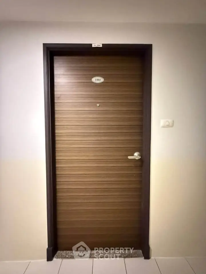 Modern apartment door with sleek wooden finish and metallic handle in a well-lit hallway.
