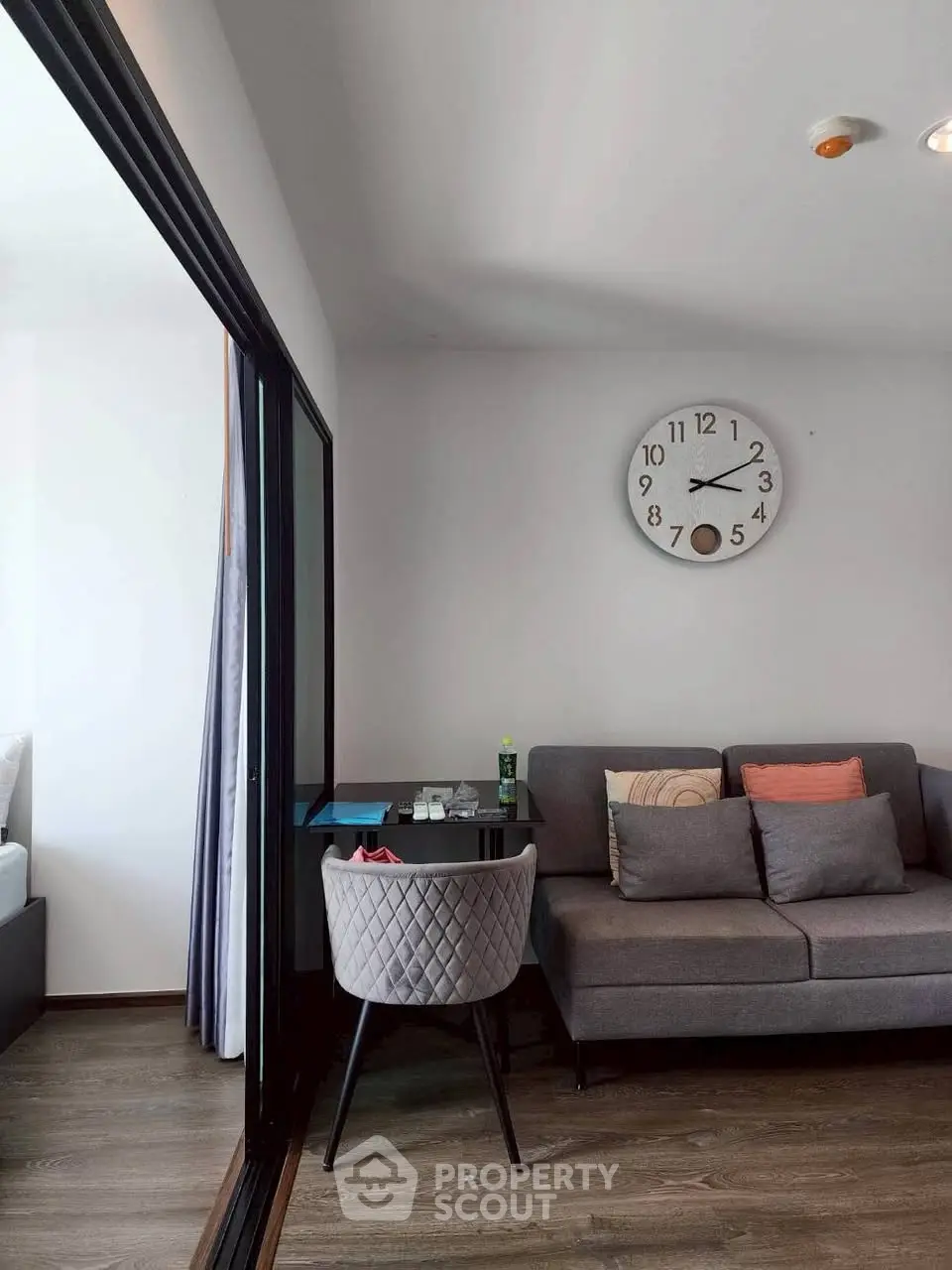 Modern living room with stylish gray sofa and wall clock, featuring a cozy dining area.
