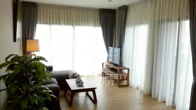Elegant living room with large windows, sheer curtains, and modern furniture.