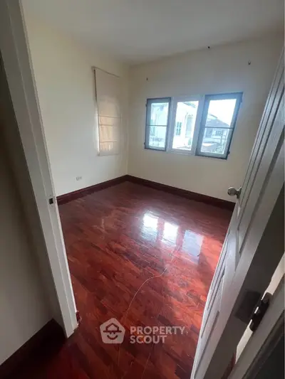 Spacious empty room with polished wooden floors and large windows.