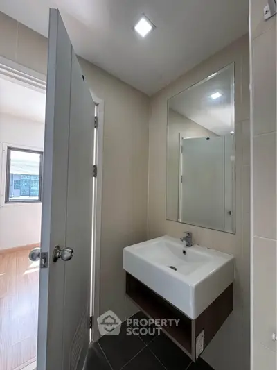 Modern bathroom with sleek sink and large mirror, featuring natural light from window.