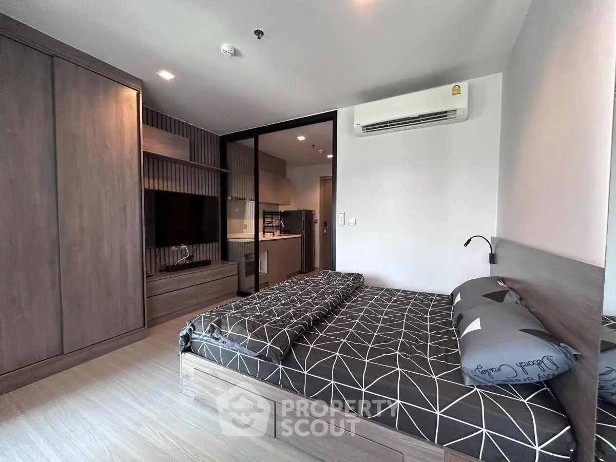 Modern bedroom with sleek design, featuring built-in wardrobe and cozy bed, adjacent to a compact kitchen area.