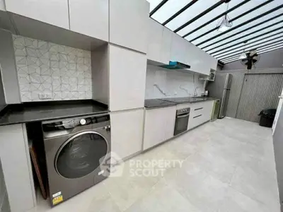 Modern kitchen with sleek appliances and open layout, featuring a washing machine and stylish backsplash.