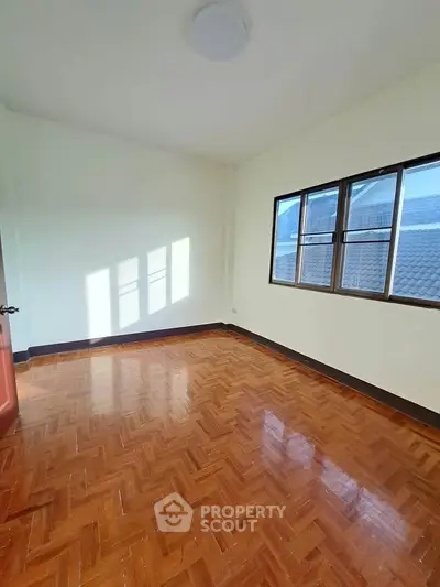 Bright empty room with polished wooden floors and large window, perfect for customization.