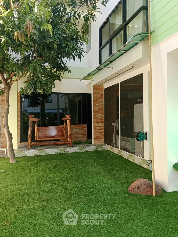 Charming garden area with lush artificial grass and cozy wooden swing, perfect for relaxation.