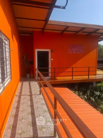 Vibrant orange exterior of modern home with elevated walkway and lush surroundings.