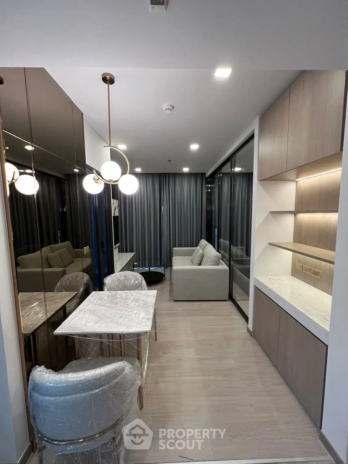 Modern living room with elegant lighting and mirrored wall, featuring a cozy sofa and dining area.