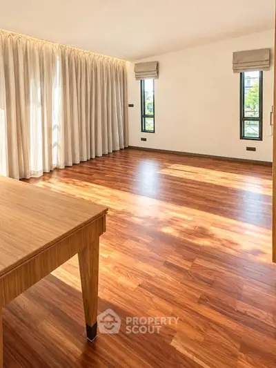Spacious empty room with wooden flooring and large windows for natural light.