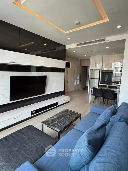 Modern living room with sleek design, featuring a large TV, stylish furniture, and open kitchen layout.