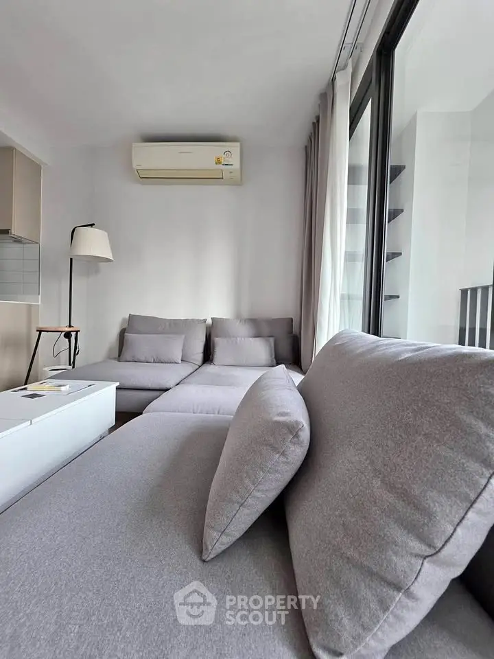 Modern living room with sleek gray sofa and air conditioning, featuring large windows for natural light.