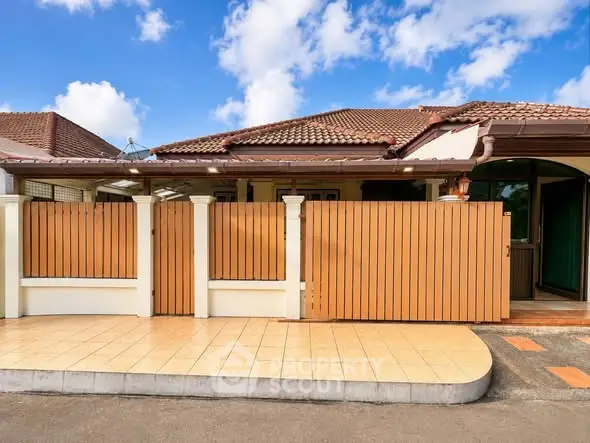 Charming single-story house with tiled roof and wooden fence under a bright blue sky.