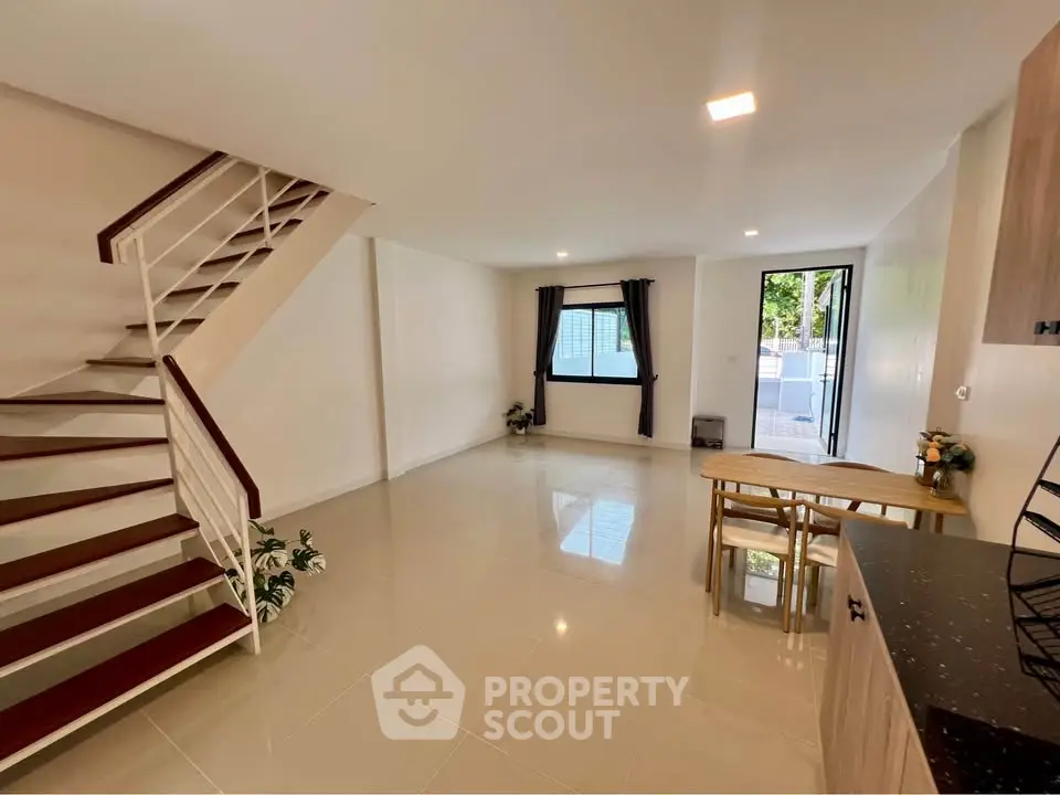 Spacious modern living room with staircase and dining area, featuring sleek tile flooring and natural light.