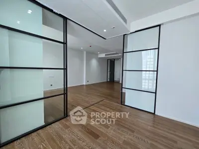 Spacious modern living room with sleek glass partitions and elegant wooden flooring.