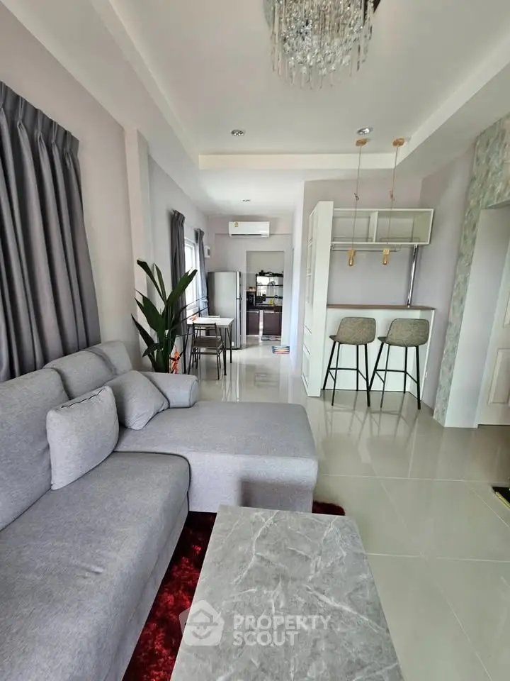 Modern living room with elegant gray sofa, stylish bar stools, and open kitchen layout.