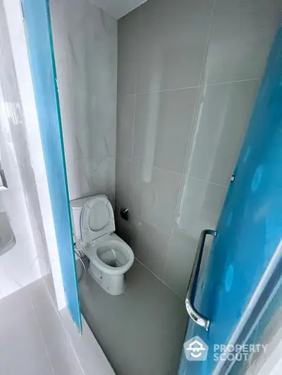 Compact modern bathroom with pristine white tiles and a convenient layout, featuring a toilet and a glass shower partition.