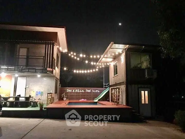 Charming pool villa with string lights and modern architecture at night.