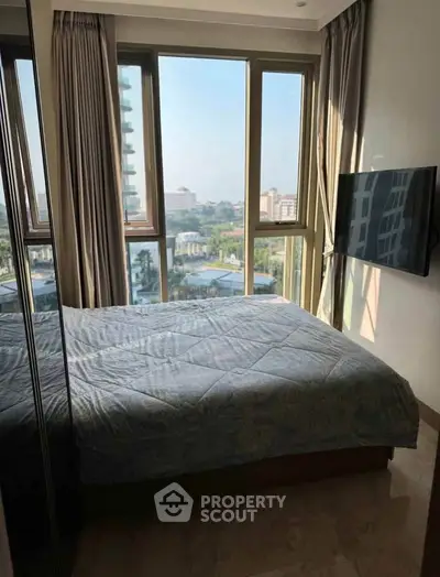 Modern bedroom with large windows offering a stunning city view, featuring a wall-mounted TV and elegant decor.