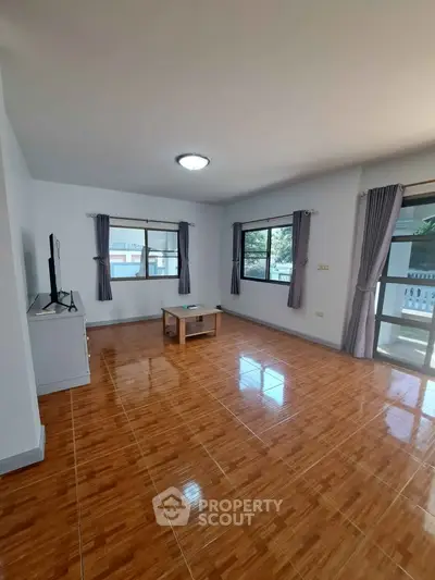 Spacious living room with large windows and polished wooden floors.