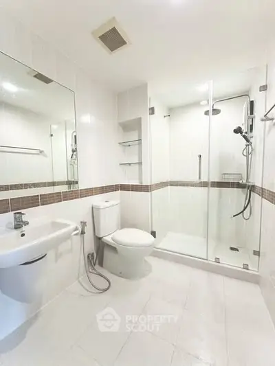 Modern bathroom with glass shower and sleek fixtures in a bright, white-tiled space.