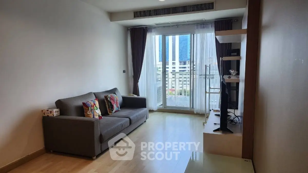 Modern living room with city view, featuring sleek furniture and natural light through large windows.