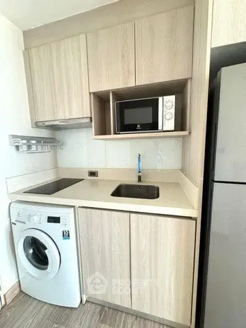 Compact modern kitchen with washing machine, microwave, and sleek cabinetry in a stylish apartment.