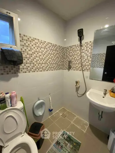 Compact bathroom with modern fixtures and mosaic tile accents, featuring a shower and small window for natural light.